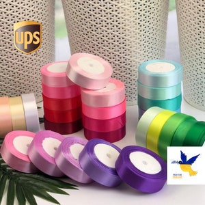 May include: Assortment of colorful satin ribbon spools in various shades of pink, purple, blue, green, and yellow. The ribbon is arranged in stacks and is ready to be used for crafting, gift wrapping, or decorating.