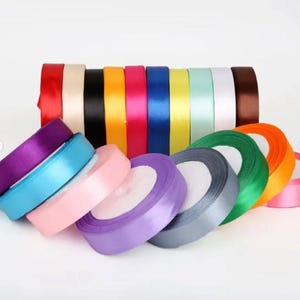 May include: A collection of satin ribbon rolls in a wide variety of colors including red, black, yellow, pink, blue, green, purple, and white. The rolls are arranged in a horizontal row and a semi-circle, showcasing the smooth, shiny texture.