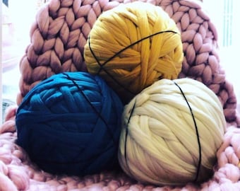 May include: Three large balls of yarn in different colors: yellow, blue, and white. The yarn is arranged on a pink knitted blanket.