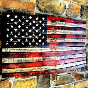 May include: A rustic American flag made of reclaimed wood with a distressed finish. The flag is painted in red, white, and blue with a weathered look. The stars are white and the stripes are red and white.