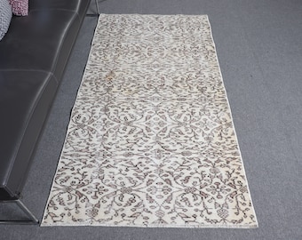 May include: A rectangular runner rug featuring an intricate, repeating floral and vine pattern in shades of dark brown and muted red against a cream-colored background. The rug has a finished edge and a low-pile texture throughout its surface.