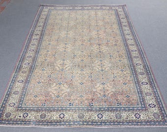 May include: A rectangular area rug featuring a beige field with an intricate all-over pattern of floral motifs and geometric shapes in shades of blue, pink, and cream. The rug is framed by a wide, detailed border with repeating floral designs.