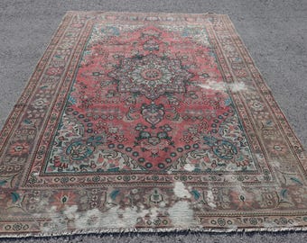 Könnte beinhalten: Ein rechteckiger Teppich mit einem zentralen Blumenmedaillon auf einem verblassten korallenroten Grund. Der Teppich zeigt komplexe florale Muster in Blaugrün, Creme und Braun, mit einer breiten dekorativen Bordüre und sichtbaren Abnutzungserscheinungen.