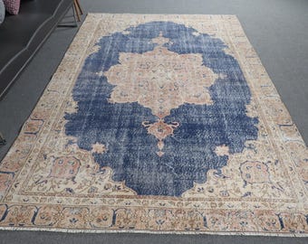 Könnte beinhalten: Ein großer rechteckiger Teppich mit einem tiefblauen Mittelfeld und einem markanten, kunstvollen floralen Medaillon in sanften Beige- und zarten Rosatönen. Der breite Rand zeigt ein komplexes Muster aus Ranken und Blumenmotiven in Beige.