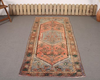 May include: A rectangular area rug featuring a central hexagonal medallion in muted blue surrounded by a field of salmon pink. The rug displays intricate geometric and floral patterns in shades of green, cream, and brown, framed by a decorative border.