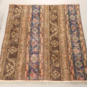 May include: A rectangular, vintage rug with a distressed look. It has vertical stripes in brown, beige, and blue, with floral and geometric patterns. The rug has a fringed edge and is likely made of woven material.