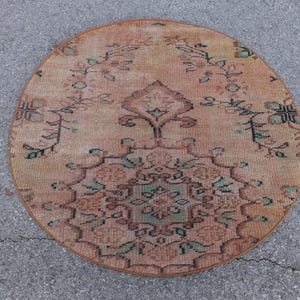 May include: A round rug featuring a faded peach and terracotta base color with a central medallion and symmetrical floral vine patterns in muted shades of sage green, dark brown, and cream, showcasing a weathered, low-pile textile construction.