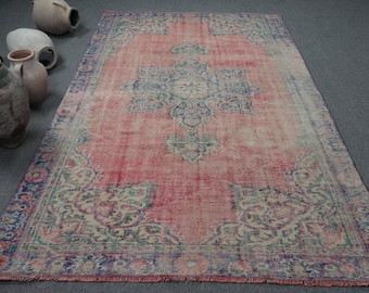 May include: A rectangular area rug featuring a faded coral pink field with a central blue and cream medallion. The border displays intricate floral patterns in shades of blue, green, and pink. The rug has short fringe along the short edges.