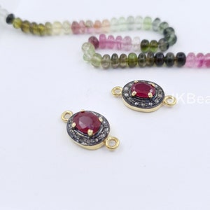 May include: Two gold-tone oval-shaped connector pieces with a red gemstone in the center and a halo of small clear gemstones around the stone. The connector pieces have a loop on each end.