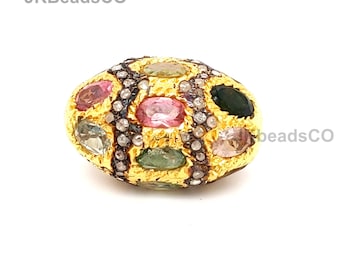 May include: A gold oval-shaped bead with a variety of colorful gemstones set in a gold frame. The bead is surrounded by a black and white diamond pattern.
