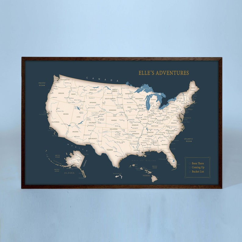 Puede incluir: Un mapa de los Estados Unidos en azul y blanco con el t&iacute;tulo "Elle's Adventures" en letras doradas. El mapa est&aacute; enmarcado en un marco de madera oscura. El texto "Been There, Coming Up, Bucket List" est&aacute; en la esquina inferior derecha.