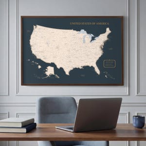 Puede incluir: Un mapa de pared enmarcado de los Estados Unidos de América con un fondo azul marino oscuro y una masa terrestre de color beige claro. El mapa incluye fronteras estatales detalladas, ciudades y el texto UNITED STATES OF AMERICA en letras doradas.