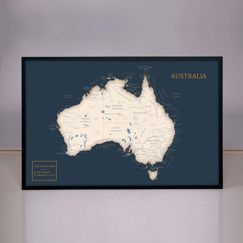 May include: A navy blue framed map of Australia with white lines showing the rivers and coastlines. The map is titled "Australia" in gold lettering. The text "The Smith Family" is in the bottom left corner with a list of "Past Adventures" and "Adventures to Come" in gold lettering.