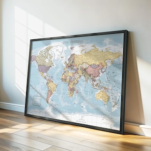 May include: A framed world map with a black border. The map shows a light blue ocean and colourful continents. The text "OUR TRAVELS" is at the top. The map is leaning against a white wall on a wooden floor.