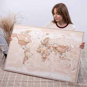 May include: A large, framed world map with a neutral color palette of beige and brown. The map is detailed, showing continents, countries, and geographical features. The frame is a light wood color.