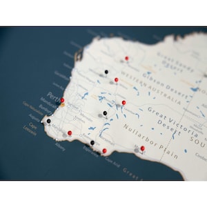 May include: A map of Western Australia with red and black push pins marking various locations. The map is on a dark blue background.