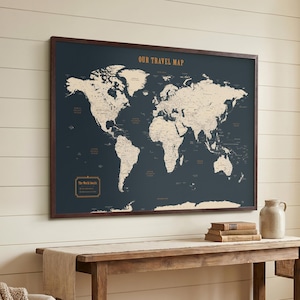 Op de afbeelding: Een wereldkaart met een donkerblauwe achtergrond en een bruine houten lijst. De kaart toont continenten in crème met contouren van landen. De tekst "OUR TRAVEL MAP" staat bovenaan. De tekst "The World Awaits" staat onderaan.