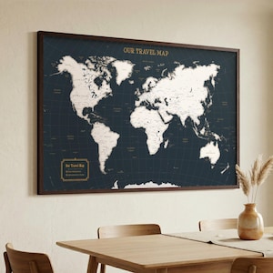 May include: A rectangular framed world map with a dark navy blue background and white continents. The text "OUR TRAVEL MAP" is printed in gold at the top centre. A gold-bordered legend box in the bottom left corner contains the text "Our Travel Map".