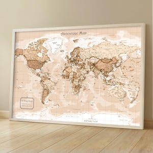 May include: A framed world map with a vintage aesthetic. The map features a sepia-toned color palette with detailed geographical information. The title "Adventure Map" is displayed at the top. The map is set against a light beige background and framed in white.