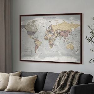 May include: A rectangular wall art print titled Adventure Map featuring a detailed world map in muted tones of beige, gray, and soft colors. The map is enclosed in a dark brown frame and displays continents, oceans, and grid lines clearly.