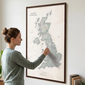 May include: A framed wall map of the United Kingdom featuring a muted sage green landmass against a cream background. The map displays geographical labels, the text "UNITED KINGDOM" at the top, and a legend at the bottom labelled "Our Travel Map".