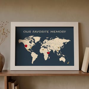 May include: A framed world map print with a dark blue background and beige continents. The text OUR FAVORITE MEMORY is printed at the top. The map features a red house-shaped pin, a red heart-shaped pin, and several small gold pins.