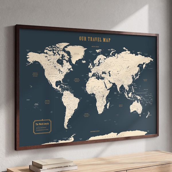 May include: A framed world map with a dark blue background and cream-colored landmasses. The text OUR TRAVEL MAP is printed at the top in gold. A rectangular legend in the bottom left corner features the text The World Awaits.