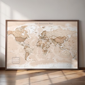 May include: A framed world map with a vintage aesthetic. The map is in shades of brown and beige, with detailed geographical features and country names. The title "Our Adventure Map" is at the top. The frame is a dark brown color.