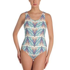 May include: A one-piece swimsuit featuring a repeating pattern of stylized feather shapes in shades of blue, purple, and beige. The swimsuit has a scoop neckline and a sleeveless design. The fabric appears to be a smooth, printed material.
