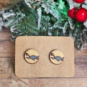 May include: A pair of wooden earrings with a gray plesiosaur design on a brown card.