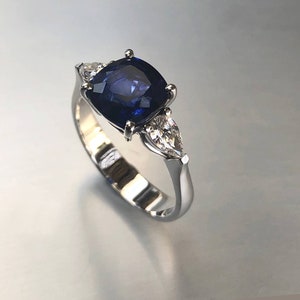 May include: A silver ring with a large, dark blue, cushion-cut sapphire and two pear-shaped diamonds.