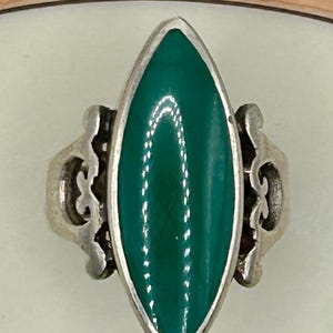 May include: A silver ring with a green oval-shaped stone set in a delicate filigree design.