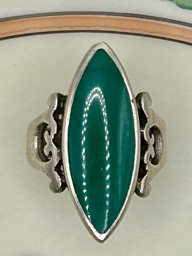 May include: A silver ring with a green oval-shaped stone set in a delicate filigree design.