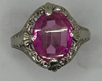 May include: A silver ring with an oval-shaped pink gemstone set in a filigree design.