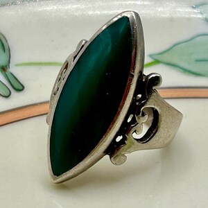 May include: A silver ring with a green gemstone set in a marquise shape. The ring has a delicate, ornate design.