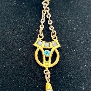 May include: Vintage gold-tone brooch with a dangling pendant. The brooch features a turquoise-colored stone and a teardrop-shaped pearl. The design includes chain links and geometric shapes, creating an elegant and classic look.