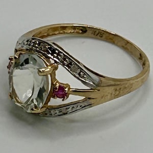 May include: A gold ring with a large oval-shaped clear gemstone, two small pink gemstones, and a band of small diamonds.