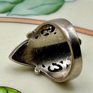 May include: Silver ring with an ornate design. The ring is shaped like a pointed oval and has a detailed, openwork pattern. The ring is shown from the underside.