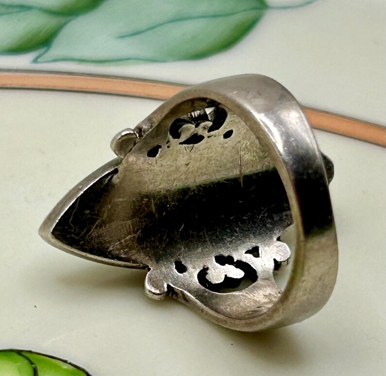 May include: Silver ring with an ornate design. The ring is shaped like a pointed oval and has a detailed, openwork pattern. The ring is shown from the underside.