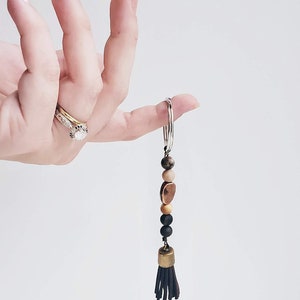 May include: A brown leather tassel keychain with wooden and metal beads. The keychain is attached to a silver key ring.