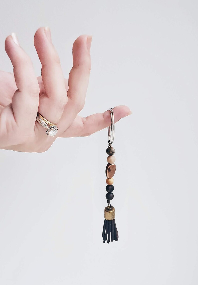 May include: A brown leather tassel keychain with wooden and metal beads. The keychain is attached to a silver key ring.
