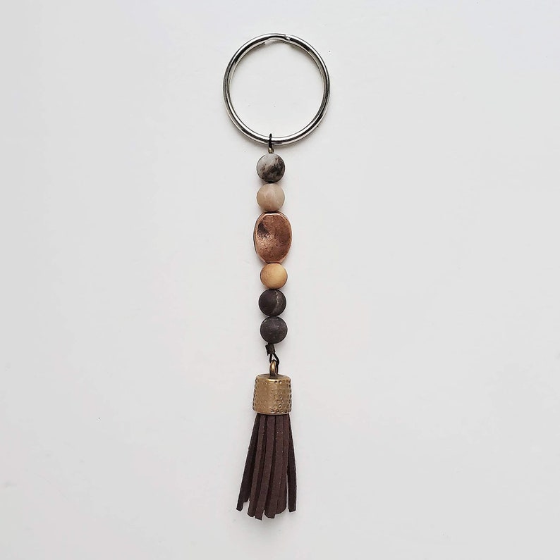 May include: A silver key chain with a brown leather tassel and a variety of brown, beige, and copper colored beads.
