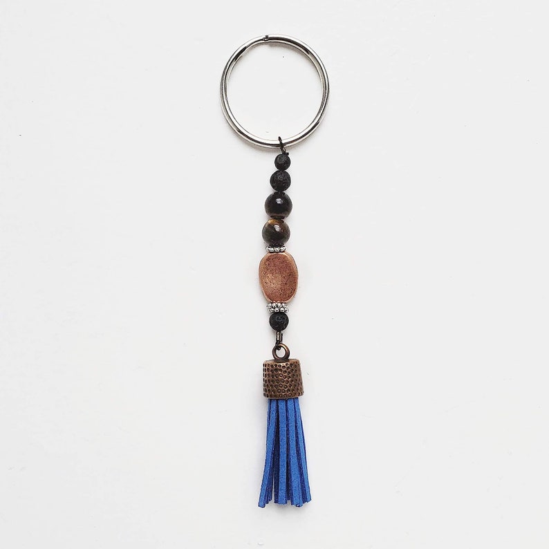 May include: A blue tassel keychain with a silver ring, brown and black beads, and a copper-colored charm.