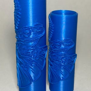 May include: Two cylindrical blue rollers featuring a raised, embossed design of a frog with detailed skin texture and webbed feet. The rollers are hollow, open at the top, and display a consistent, vibrant blue color throughout their structure.
