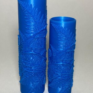 May include: Two cylindrical blue rollers featuring a raised, textured pattern of fern leaves and circular floral motifs. These tools have a smooth, hollow interior and a detailed exterior surface designed for creating impressions in soft materials.