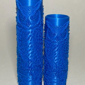 May include: Two cylindrical blue rollers featuring a raised, embossed pattern of an owl perched on a branch. The rollers are hollow and open at the top, with a smooth interior surface and a detailed, textured exterior design of feathers and leaves.