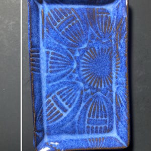 May include: A rectangular blue ceramic tray, 6.5 inches long and 4.0 inches wide, with a raised rim and a textured floral pattern. The tray has a glossy finish and brown accents.