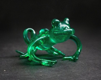 May include: A green glass frog figurine with a detailed design. The frog is sitting on a black surface.