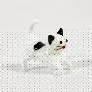 May include: A white glass cat figurine with black markings and a red nose. The cat is in a playful pose with its tail raised.