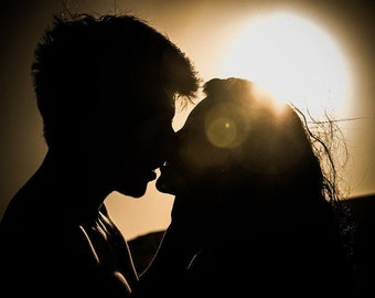 May include: Silhouette of a couple kissing at sunset, with the sun creating a bright lens flare.